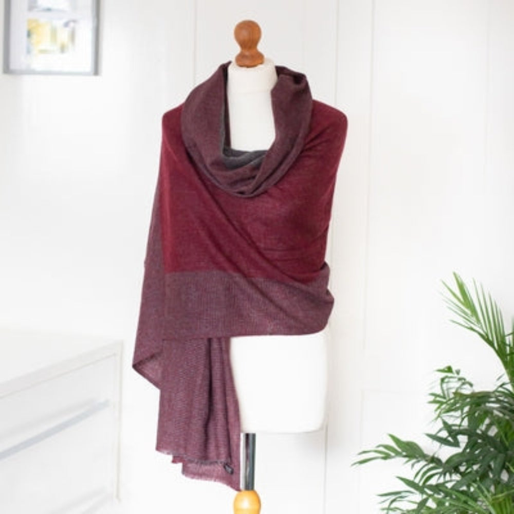 A Handwoven Cashmere Reversible Pashmina in Claret & Grey colours on a mannequin against a white background with a green plant decoration. 