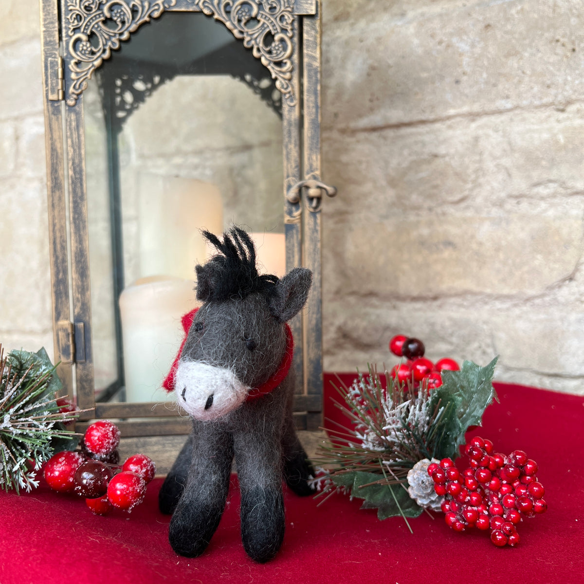 Discover the charm of our artisan, handcrafted felted wool Donkey.&amp;nbsp;

A delightful festive companion perfect for adding warmth to your seasonal décor. Each piece is handcrafted crafted from pure felted wool with hand-stitched details and dressed in a vibrant red scarf that captures the spirit of the season.

Shown against a cotswold stone wall background on gold silk fabric with festive holly and candles and decorative accents. 