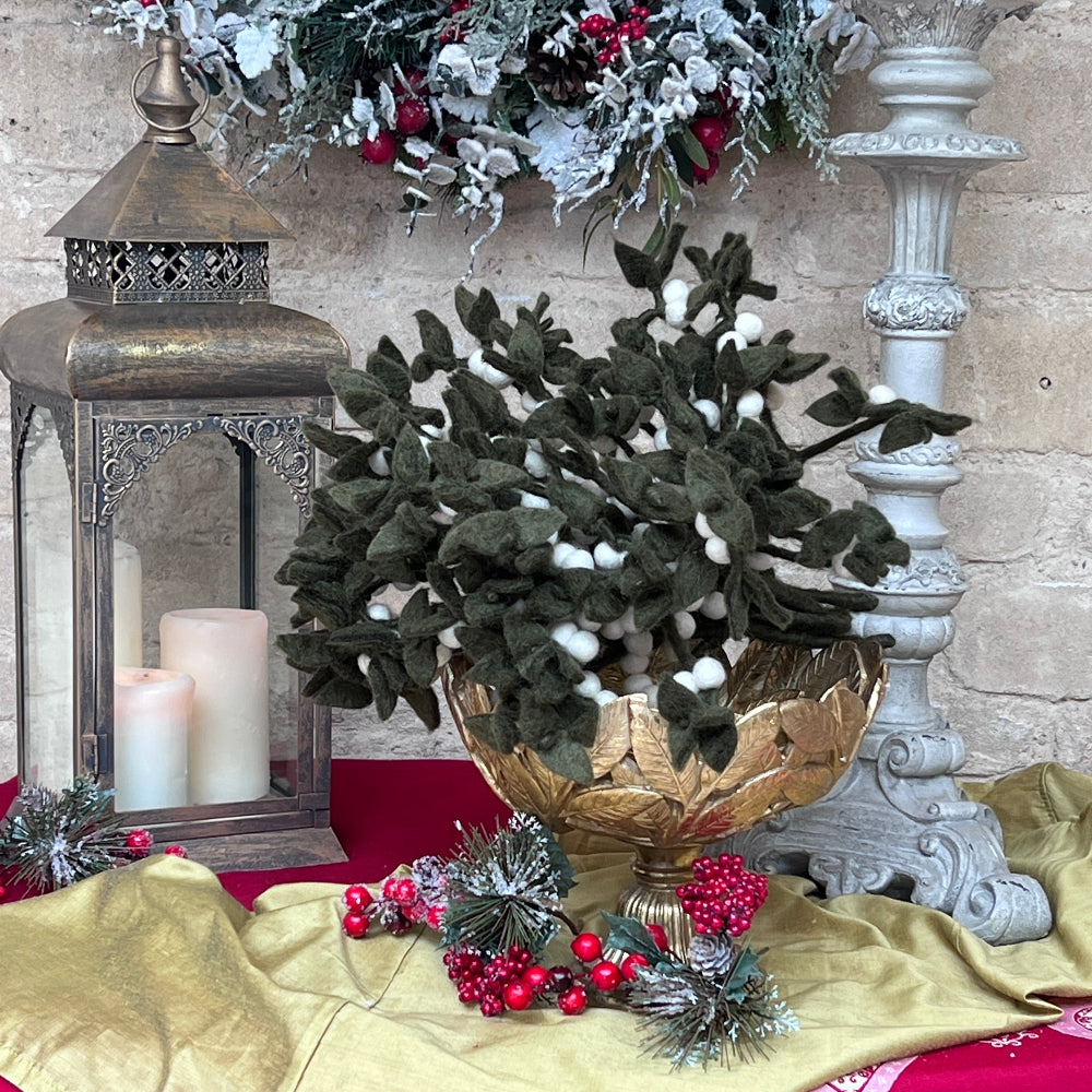 Our Mistletoe offers a refined touch to your holiday décor, perfect for creating memorable Christmas gatherings. Made from felted New Zealand wool, its pliable wired stems let you adjust the shape to suit your style.

This durable and eco-friendly ornament measures around 12" (30.48 cm) long, designed for enduring festive charm year after year. Shown in a gold decorative bowl, with candles and festive decoration against a cotswold stone wall. 