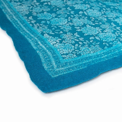 Pure Wool Felted Floral Rug. Turquoise colour in a room with decorative items and sofa on a neutral carpet.