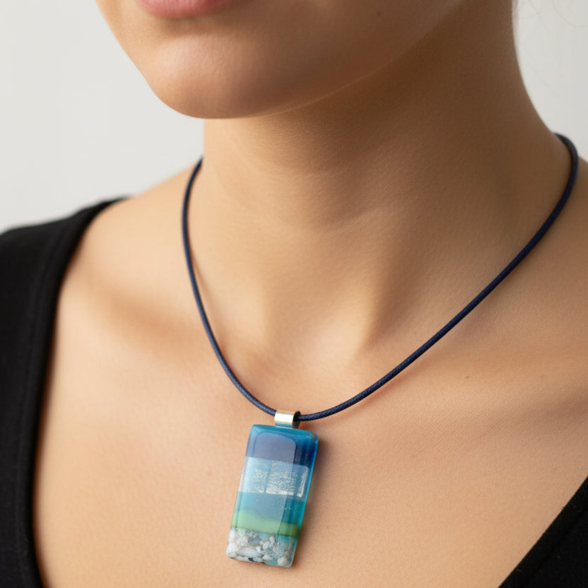 Douée -  Handcrafted Seascape Glass Pendant.  Shown against a beached piece of drift wood with a blue wax cord. 